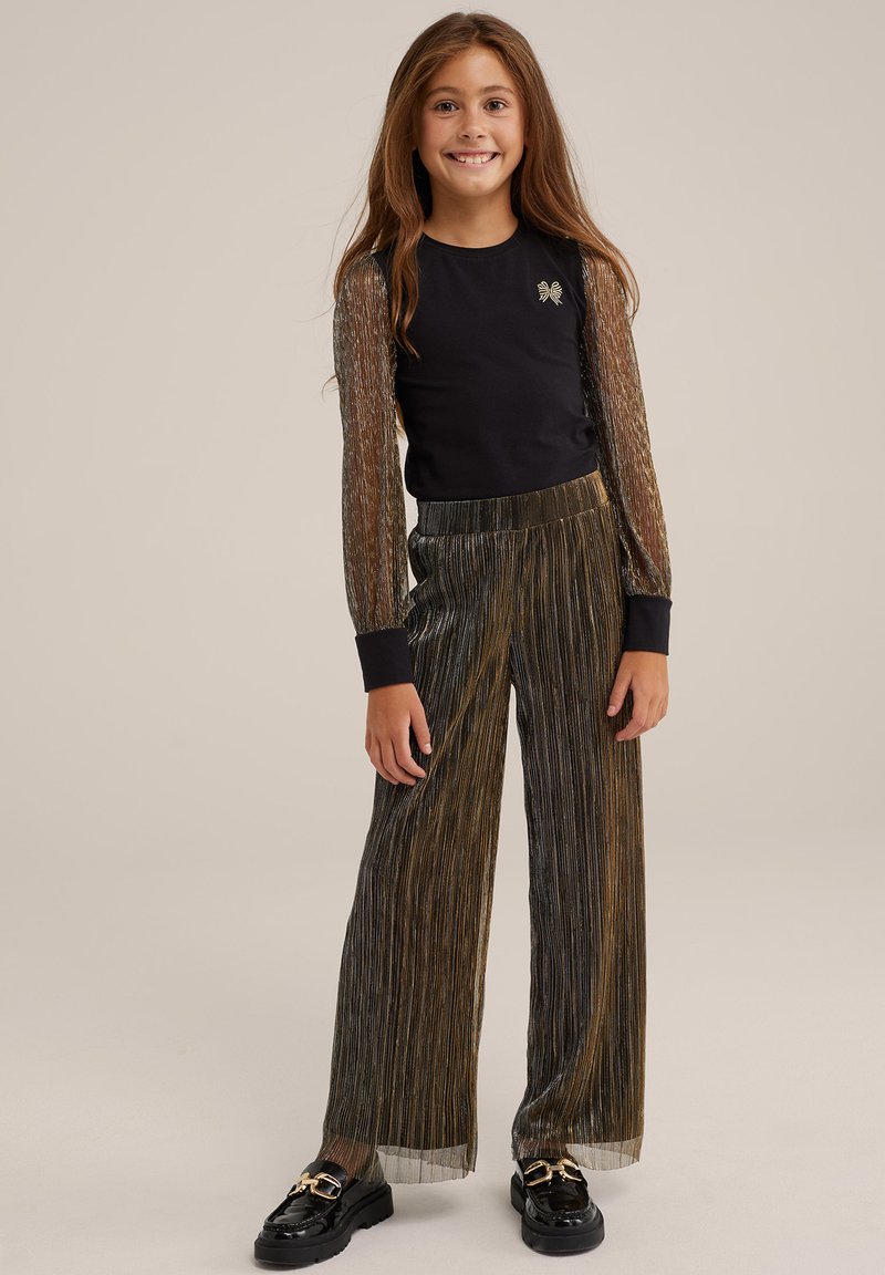 Svart långärmad topp med genomskinliga ärmar i metalltråd, matchad med guld- och svarta plisserade vida byxor. Svarta loafers med guldaccenter.