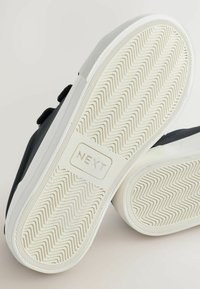 Mustad mustad musta valguseeritud kummitalla ja kalaseljaga, millel on valge vaheosa. Brändi logo "NEXT" on nähtav tallal.