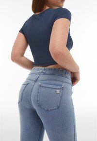 Ljusblå denimjeans med en åtsittande silhuett, elastisk midja och två bakfickor. Tyget har en slät textur med en blekt finish.