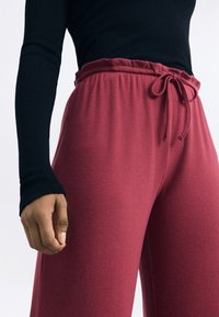 Rode geribbelde wijde broek met een trekkoord in de taille, gecombineerd met een zwart langemouwtop met aansluitende mouwen en een ronde hals.