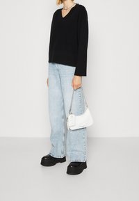 Svart v-ringad tröja, ljusblå baggyjeans, svarta kraftiga klackskor och en liten vit handväska med silverkedjesträng.