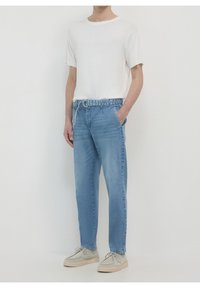 T-shirt blanc léger à col rond, associé à un jean en denim bleu clair à coupe décontractée. Chaussures beige doux à bout arrondi.