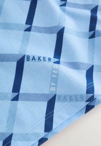 Tissu bleu clair avec motif géométrique à carreaux bleu foncé et texte "BAKER BY TED" imprimé près du bord cousu.