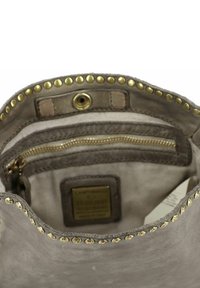 Interno della borsa in pelle grigia con borchie dorate lungo il bordo. Presenta una tasca con zip e una fodera in tessuto con l'etichetta del marchio.
