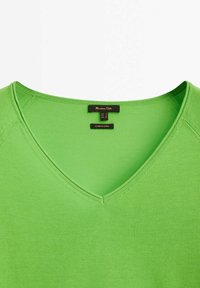 T-shirt vert à col en V et manches courtes avec une étiquette en tissu à l'intérieur du col indiquant la marque et la taille.