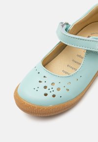 Chaussure Mary Jane en cuir bleu clair avec un design perforé, une sangle velcro et une semelle en caoutchouc texturé couleur tan.