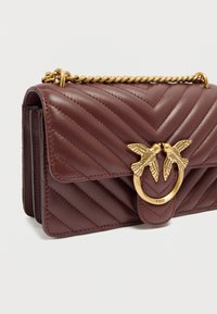 Μπορντό δερμάτινη τσάντα χειρός με ραβδώσεις σε σχήμα σέβρον, χρυσή αλυσίδα ιμάντα και διακοσμητικό κούμπωμα με δύο σχέδια πουλιών.