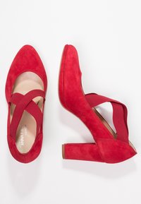 Chaussures à talons hauts en suede rouge avec un design à lanières croisées. Les talons sont en forme de bloc, et les chaussures présentent un intérieur lisse.