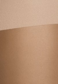 Collant beige senza cuciture con un design a coste testurizzato. La parte superiore è di un beige chiaro, mentre la parte inferiore presenta una tonalità più scura.