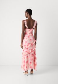 Pink floral dress with sheer ruffles, backless design, tiered layers, and knee-length hem, featuring a lightweight, flowing fabric.