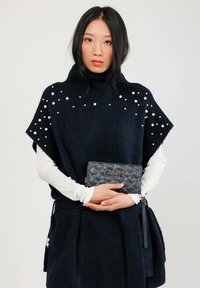 Poncho in lana navy con colletto alto, decorato con perline bianche alle spalle, abbinato a una pochette nera trapuntata con dettagli dorati.