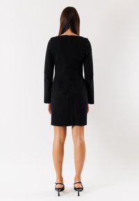 Abito nero a maniche lunghe con scollatura quadrata e silhouette aderente, dotato di zip sul retro e tessuto liscio.