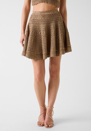 Mini-jupe évasée marron en crochet portée avec un haut assorti et des sandales beiges à talons hauts à brides, jambes visibles à partir du milieu du corps vers le bas.
