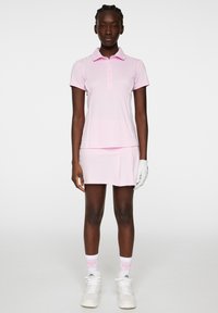 Rosa polo skjorta med krage, korta ärmar och knapplist, i kombination med en matchande plisserad kjol. Vita handskar och sneakers ingår.