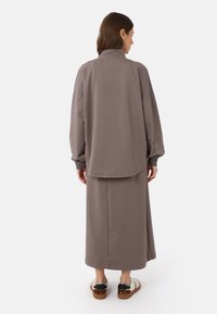 Grau Baumwoll-Loungewear-Outfit mit einem übergroßen Sweatshirt mit hohem Kragen und einem langen Rock, kombiniert mit mehrfarbigen gemusterten Schuhen.
