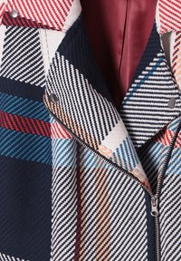 Veste zippée avec motif rayé diagonal multicolore en bleu marine, rouge, blanc, bleu et beige, avec boutons-pression et doublure intérieure bordeaux.