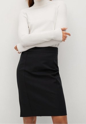 Femme portant un pull à col roulé blanc en maille côtelée et une jupe crayon noire unie longueur genou, sur un fond clair uni.