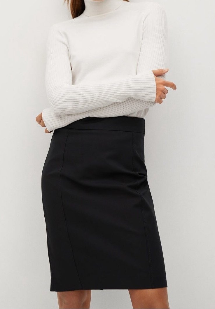 Femme portant un pull à col roulé blanc en maille côtelée et une jupe crayon noire unie longueur genou, sur un fond clair uni.