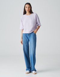 Top in magenta a maglia con maniche corte e tasca frontale, abbinato a jeans a gamba larga blu chiaro e scarpe bianche con suole in gomma.