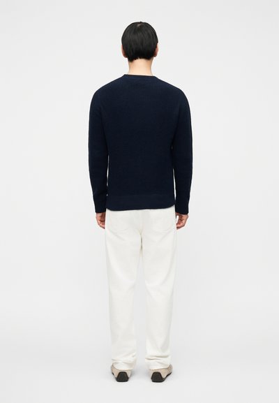 Μπλε σκούτερ πλεκτό με υφή υφής, μακριά μανίκια και ριμπ στηρίγματα. Συνδυασμένο με παντελόνια εκρού και παπούτσια ουδέτερων τόνων.