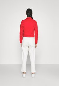 Chaqueta de mezclilla roja, diseño corto con mangas largas, combinada con pantalones anchos blancos y zapatillas blancas. Líneas simples y limpias.