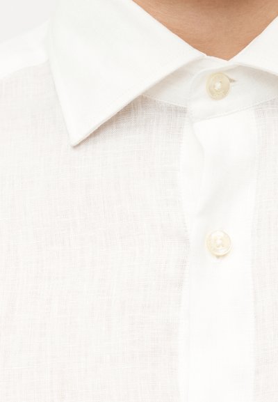 Κοντινό πλάνο ενός ατόμου που φοράει λευκό πουκάμισο από λινό με κλασικό μυτερό γιακά και εμφανή κουμπιά.