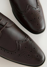 Chaussures en cuir brun avec une finition lisse, design à bouts ouverts, détails perforés et une section texturée près des lacets.