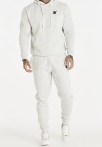 Felpa grigia chiara in pile con tasca a marsupio e logo nero, abbinata a pantaloni sportivi coordinati, con polsini elasticizzati e una vestibilità comoda.