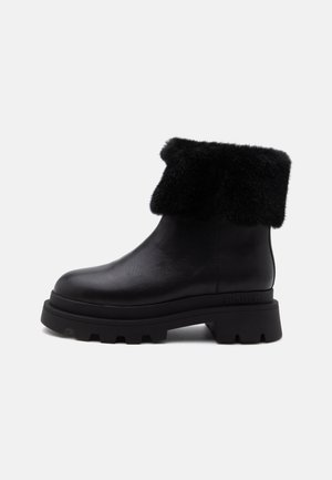 Bottine en cuir noir avec semelle à gros crampons épaisse et revers en fourrure noire replié autour du haut, vue de profil sur fond blanc.