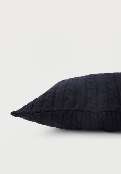 Σκούρο μπλε παραλληλόγραμμο μαξιλάρι με υφή πλεξίματος καλωδίων, εμφανιζόμενο από πλευρά, σε απλό ανοιχτό φόντο.