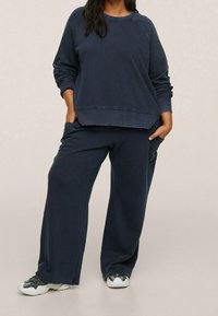 Sweatshirt décontracté bleu foncé à manches longues et col côtelé, associé à un pantalon large assorti. Le matériau semble doux avec une finition texturée.