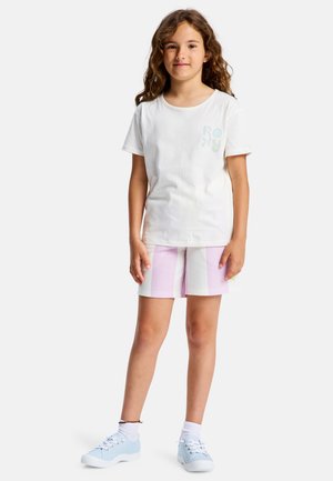 Camiseta blanca de algodón con el colorido logo "ROXY", combinada con shorts a rayas pastel en rosa y blanco. Zapatillas azules completan el conjunto.