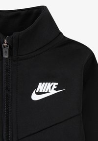 Jachetă neagră cu fermoar, cu guler înalt, material texturat și logo Nike alb pe partea stângă. Fermoar cu un mâner rezistent.