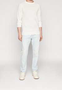 Suéter de punto blanco con puños y dobladillo acanalados, combinado con jeans azul claro y zapatillas blancas. El conjunto tiene un ajuste casual y una textura suave.