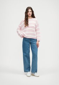 Sweater de malha listrado em rosa e branco com decote redondo, combinado com jeans de perna larga azul claro e ténis brancos.