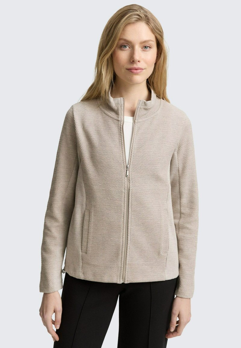 Giacca beige con zip realizzata in tessuto testurizzato; presenta un colletto alla francese e tasche laterali; taglio dritto e maniche lunghe.