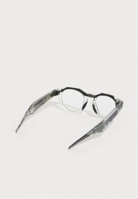 Clear eyeglasses with a black top rim, featuring transparent temples and oval lenses. Notable hinge details on the sides.