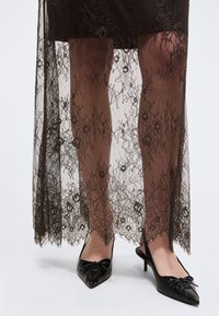 Jalad, mis kannavad musta läbipaistvast pitsist seelikut koos lillemustritega, mille all on lühem aluskiht, kombineeritud mustade terava ninaga madala kontsaga kingadega, millel on lipsukesed.