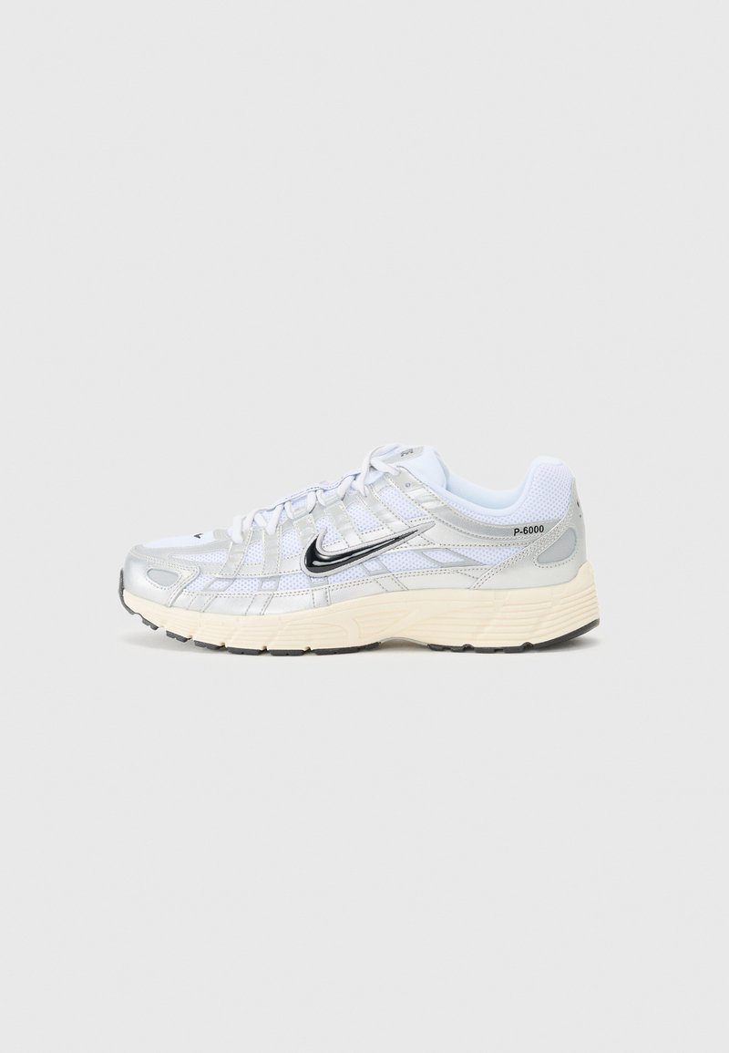Hvite mesh sneakers med sølvfarge detaljer, svart Nike swoosh, polstret krage og teksturert såle. Har en lagdelt design for stabilitet.