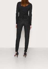 Svarta byxor med prickar, smal passform, elastisk midja och ankellång design, tillsammans med svarta högklackade sandaler.