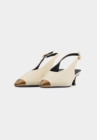 Εκρού πέδιλα slingback με μεταλλικές χρυσές μυτερές μύτες και μικρά τετράγωνα τακούνια σε λευκό φόντο.