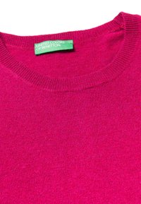 Fuksjowy sweter z dzianiny z okrągłym dekoltem i ściągaczami na rękawach. Posiada zielony metkę z napisem "UNITED COLORS OF BENETTON". Miękka tekstura.