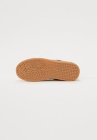 Talpa din cauciuc cu un model texturat, având un detaliu circular rotund și o culoare maro. Accentuate cu un design ondulat și trei prinderi circulare.