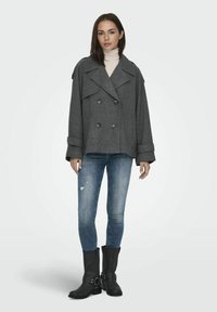Veste double boutonnage en mélange de laine grise avec larges revers, manches retournées, jean foncé assorti et bottes noires montantes avec boucles.
