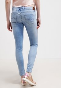 Jeans skinny de color azul claro con un acabado desgastado, dos bolsillos traseros con un patrón en forma de ola y una etiqueta de cuero marrón en la cintura.