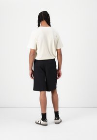 Light beige, short-sleeve t-shirt paired with black shorts, featuring a relaxed fit. Simple design with a subtle texture. Casual footwear included.