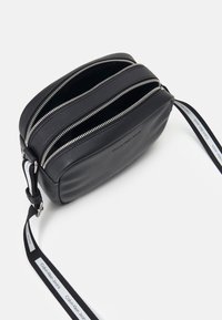 Černá kožená crossbody taška s několika oddíly, stříbrnými zipy a značkovým popruhem. Hladký povrch s obdélníkovým tvarem.