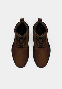 Scarpe in pelle sintetica marrone con suole in gomma nera, caratterizzate da punta rotonda, lacci frontali e linguetta sollevata per facilitarne l'indossamento.