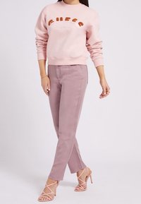 Sudadera rosa con el logo "GUESS California", combinada con jeans ajustados de color rosa claro y sandalias de tacón con tiras. Tejido suave, corte casual.