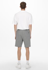 Pantaloni corti grigi realizzati in un tessuto morbido, con un design semplice e una vita elastica. Abbinati a una maglietta bianca semplice e scarpe da ginnastica bianche.